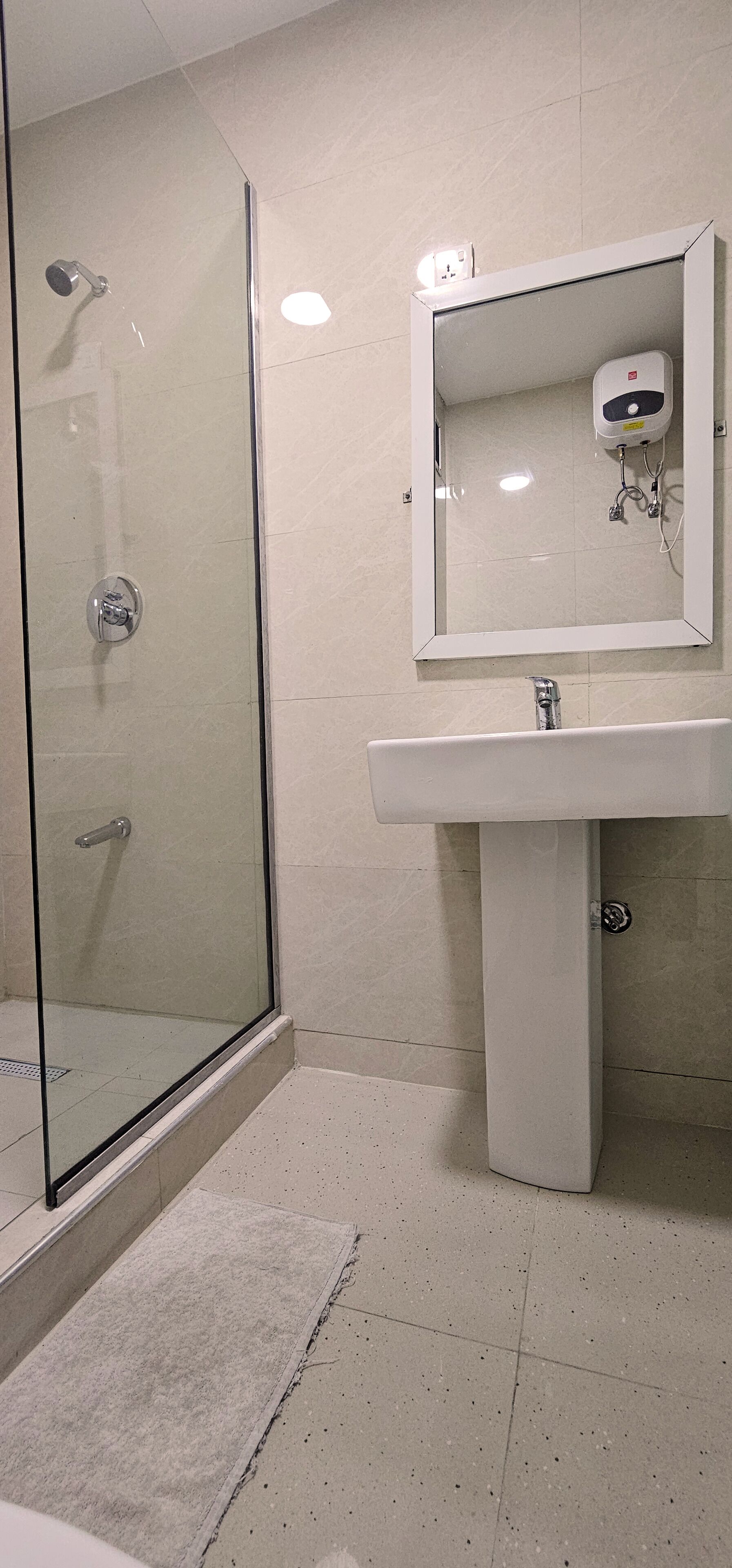 A bathroom with a glass shower enclosure, a sink with a mirror, and a hand dryer.