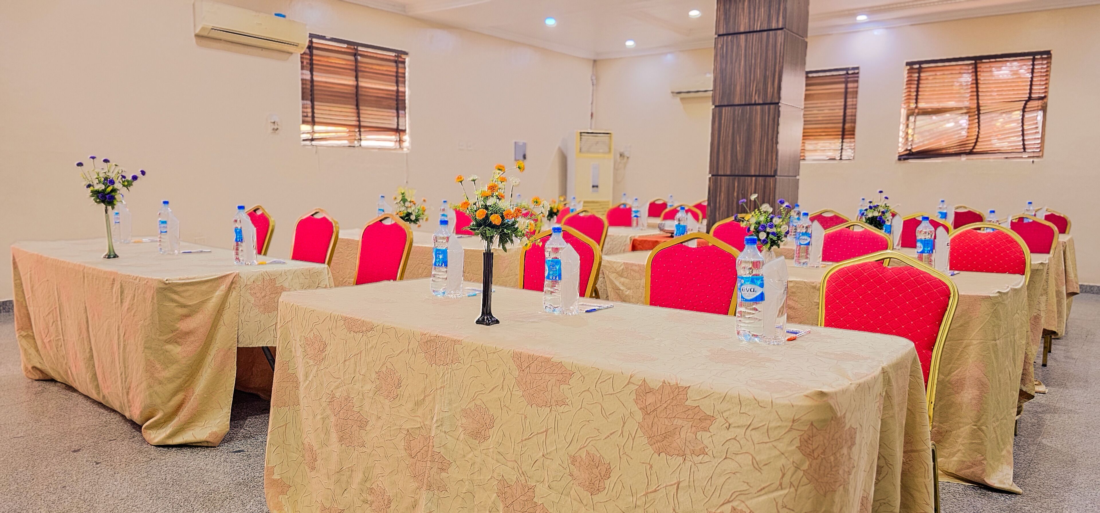 A conference room with multiple tables, red chairs, and floral centerpieces.