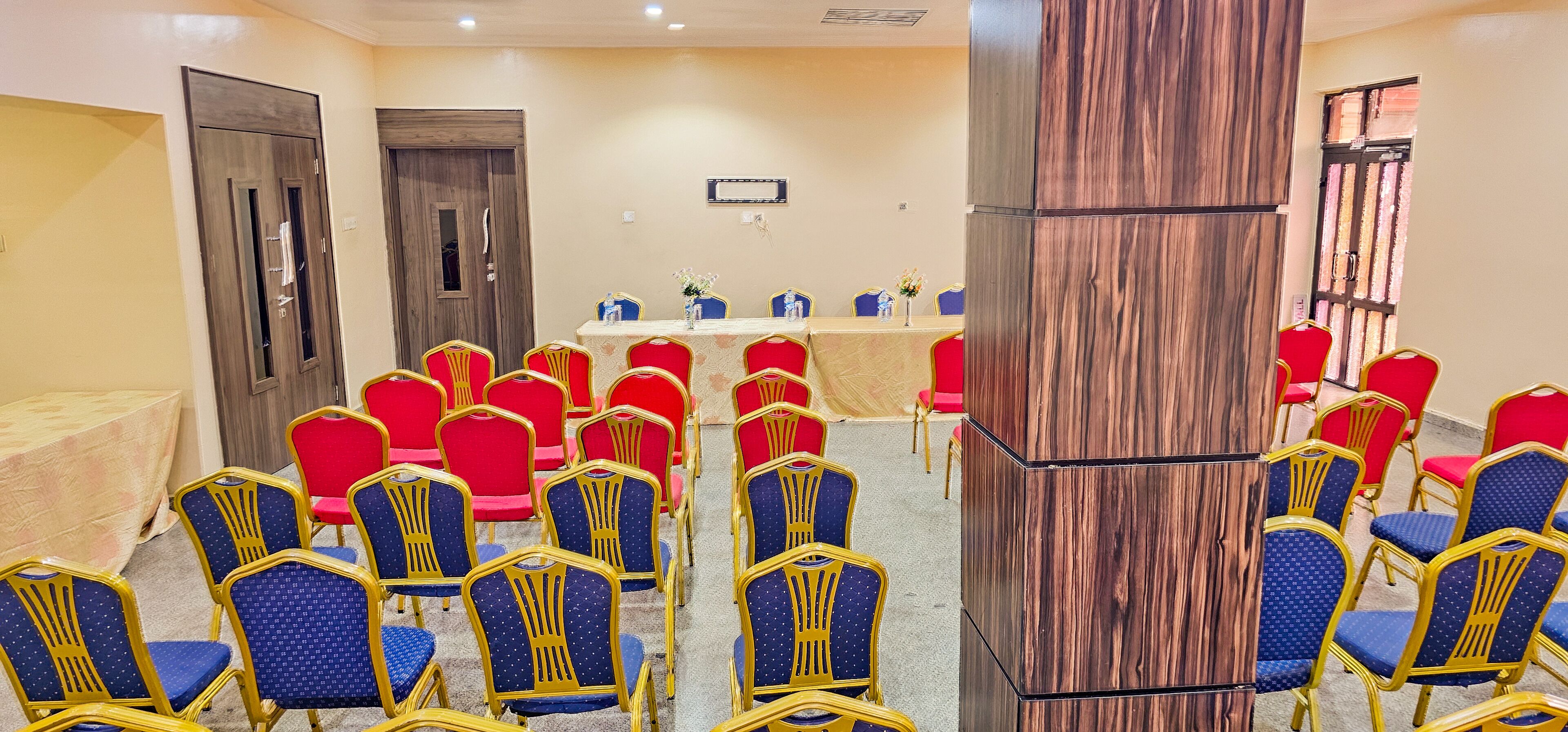 Une salle de conférence avec une longue table, des chaises rouges et bleues, et un lambris en bois.