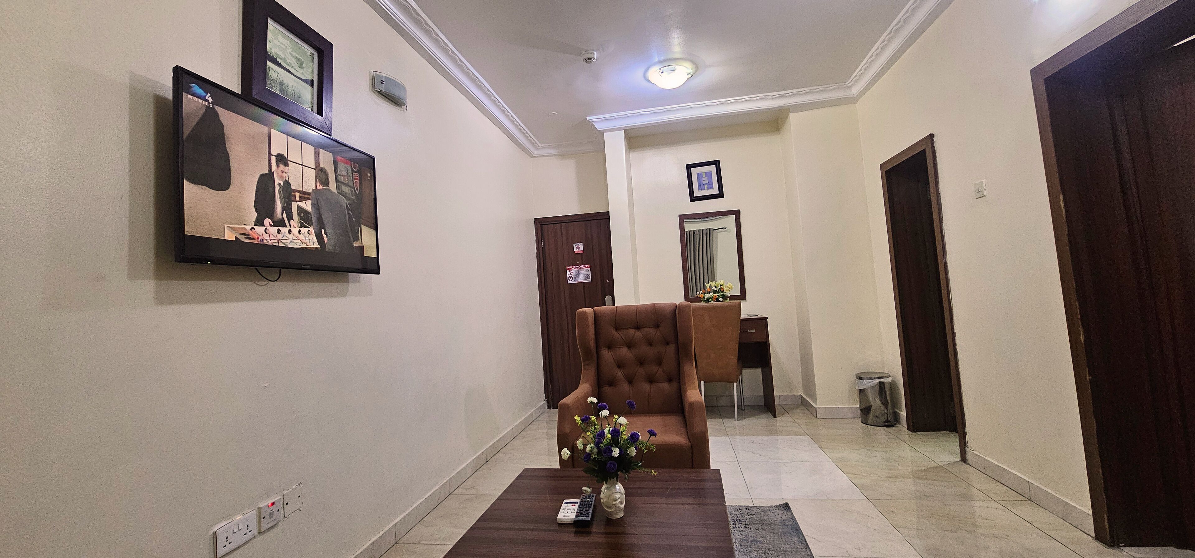A hotel lobby with a reception desk, a tufted armchair, a vase with flowers, and a framed picture on the wall.