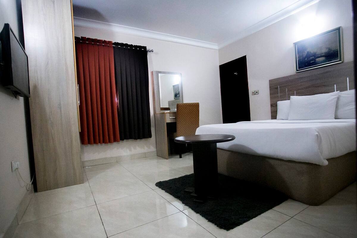 A hotel room with a bed, bedside table, TV, and a window with curtains.
