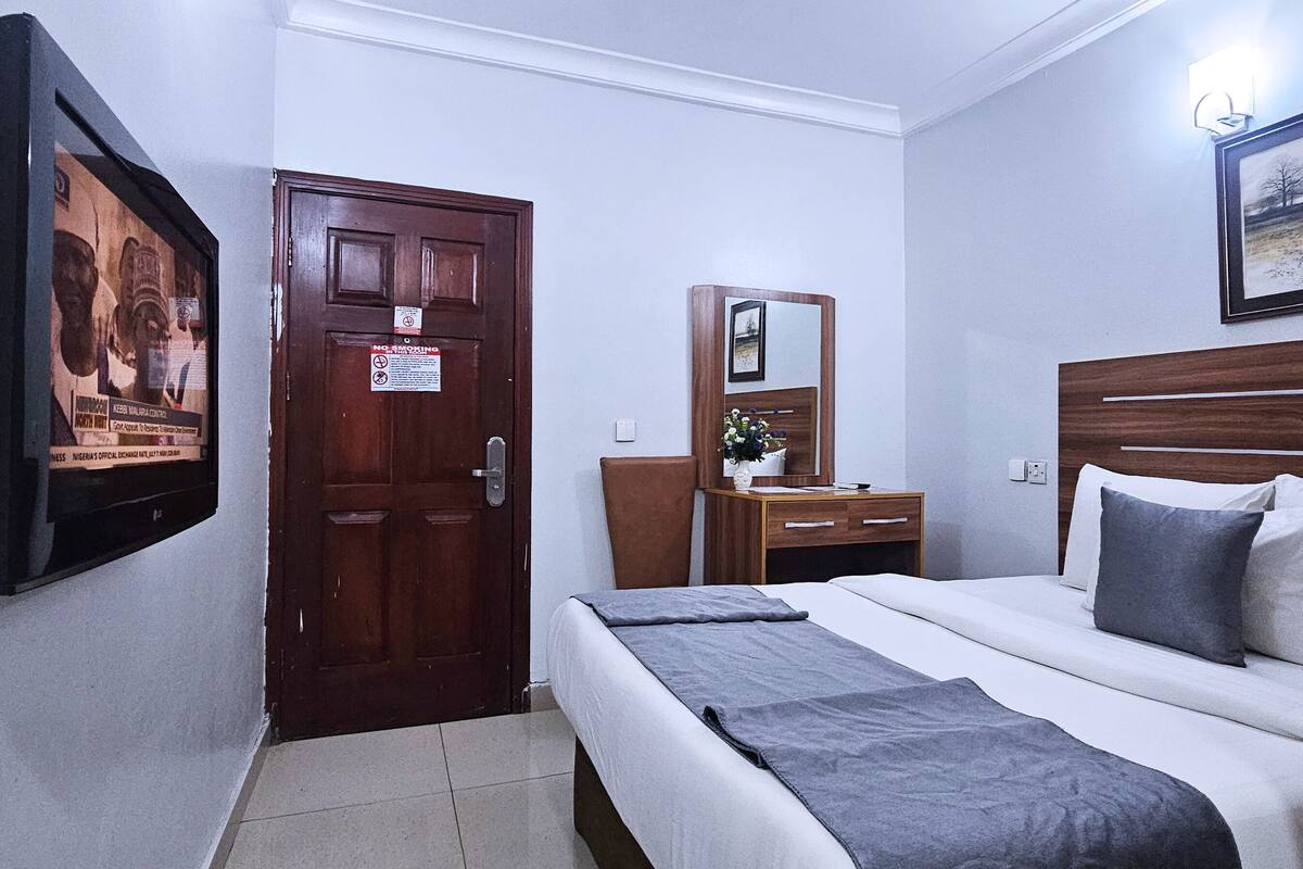 A hotel room with a bed, bedside table, mirror, and a wall-mounted TV.