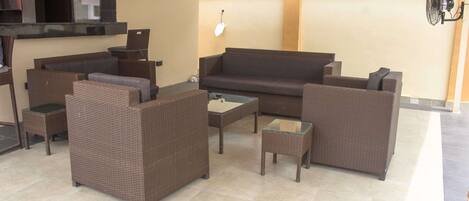 Un espace extérieur aménagé avec des meubles en osier, un canapé et une petite table, le tout abrité.