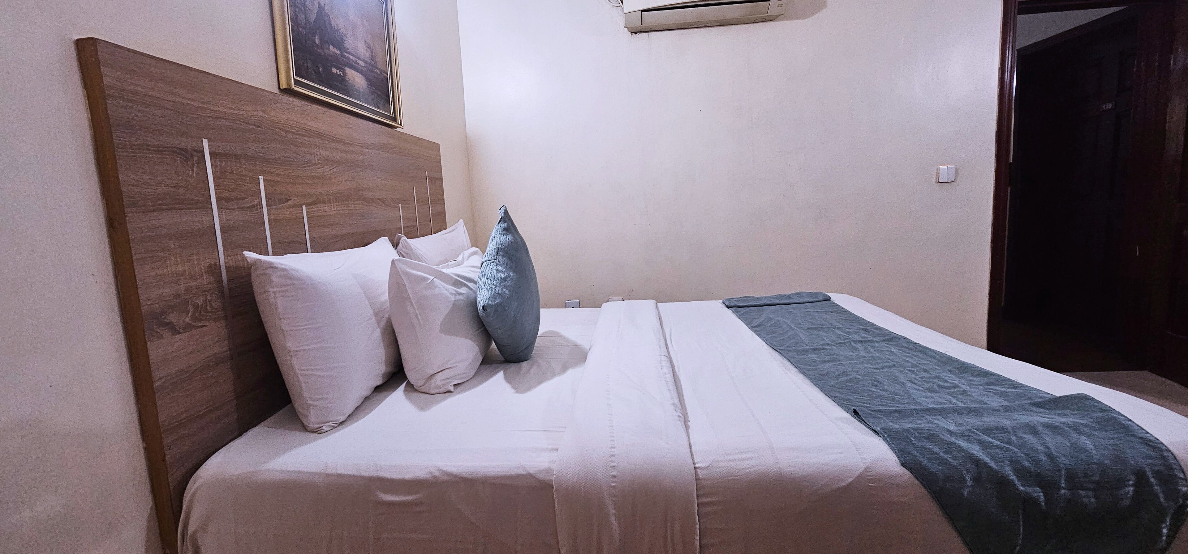 A neatly made bed with a wooden headboard, white and gray pillows, and a blue blanket.