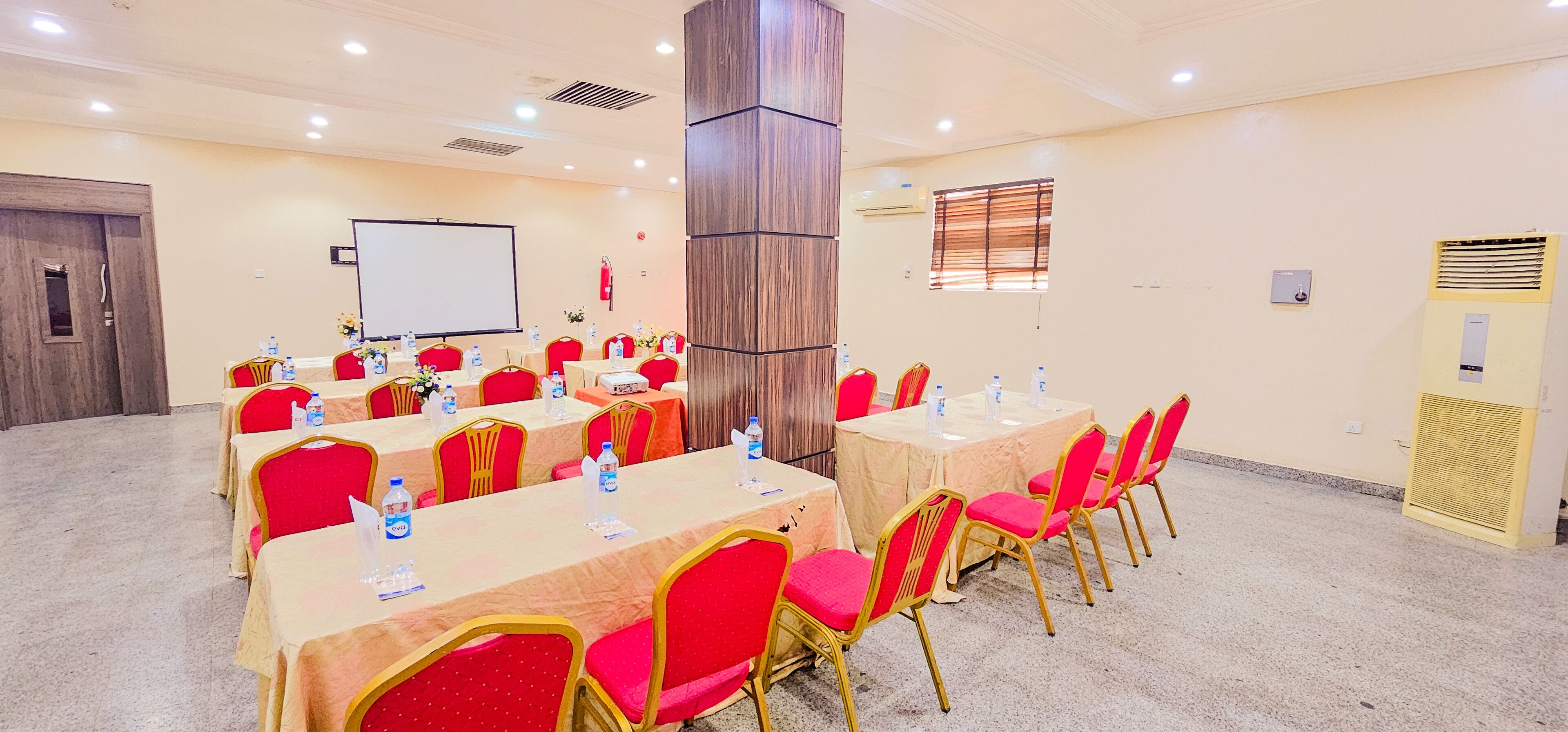 A conference room with multiple tables and chairs, equipped with water bottles and floral centerpieces.