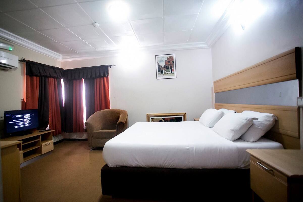A hotel room with a bed, a chair, a television, and a picture on the wall.