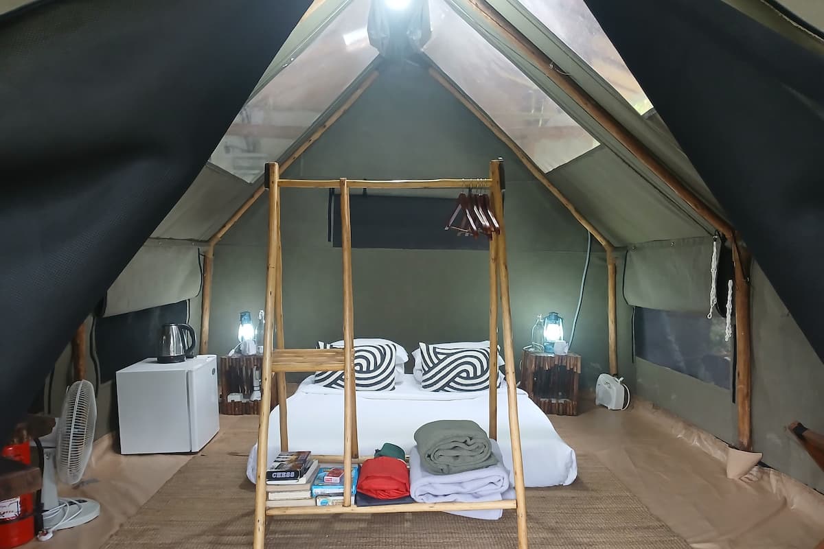 A cozy tented accommodation with a bed, bedside lamps, and a fan.