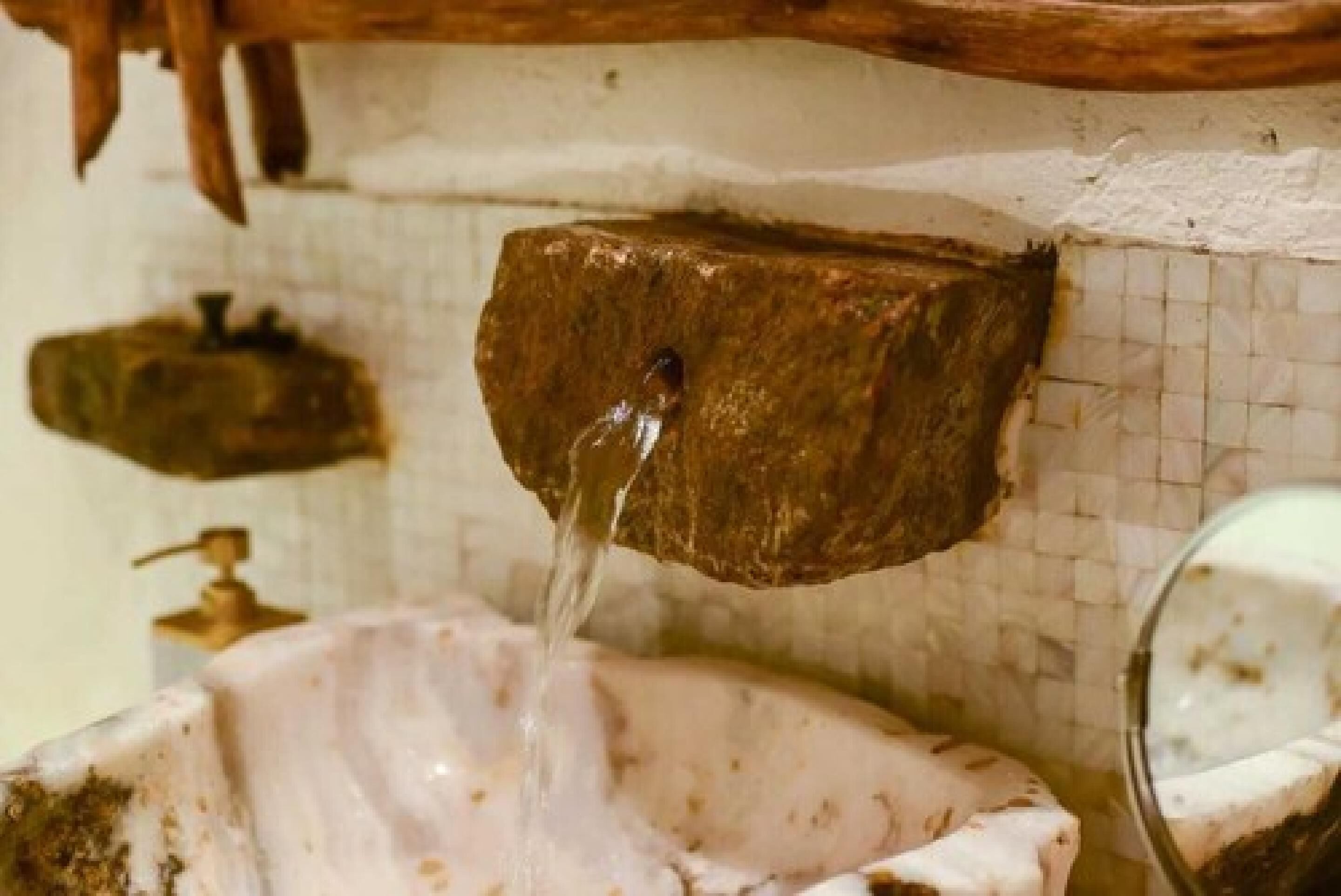 Une fontaine rustique en pierre, dont l’eau jaillit dans un bassin.