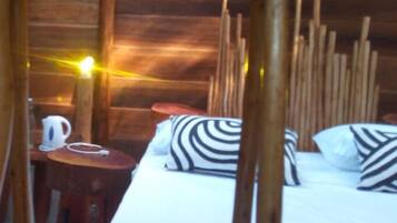 Habitación de cabaña de madera con una cama, almohadas a rayas, una mesa con un hervidor y una silla.