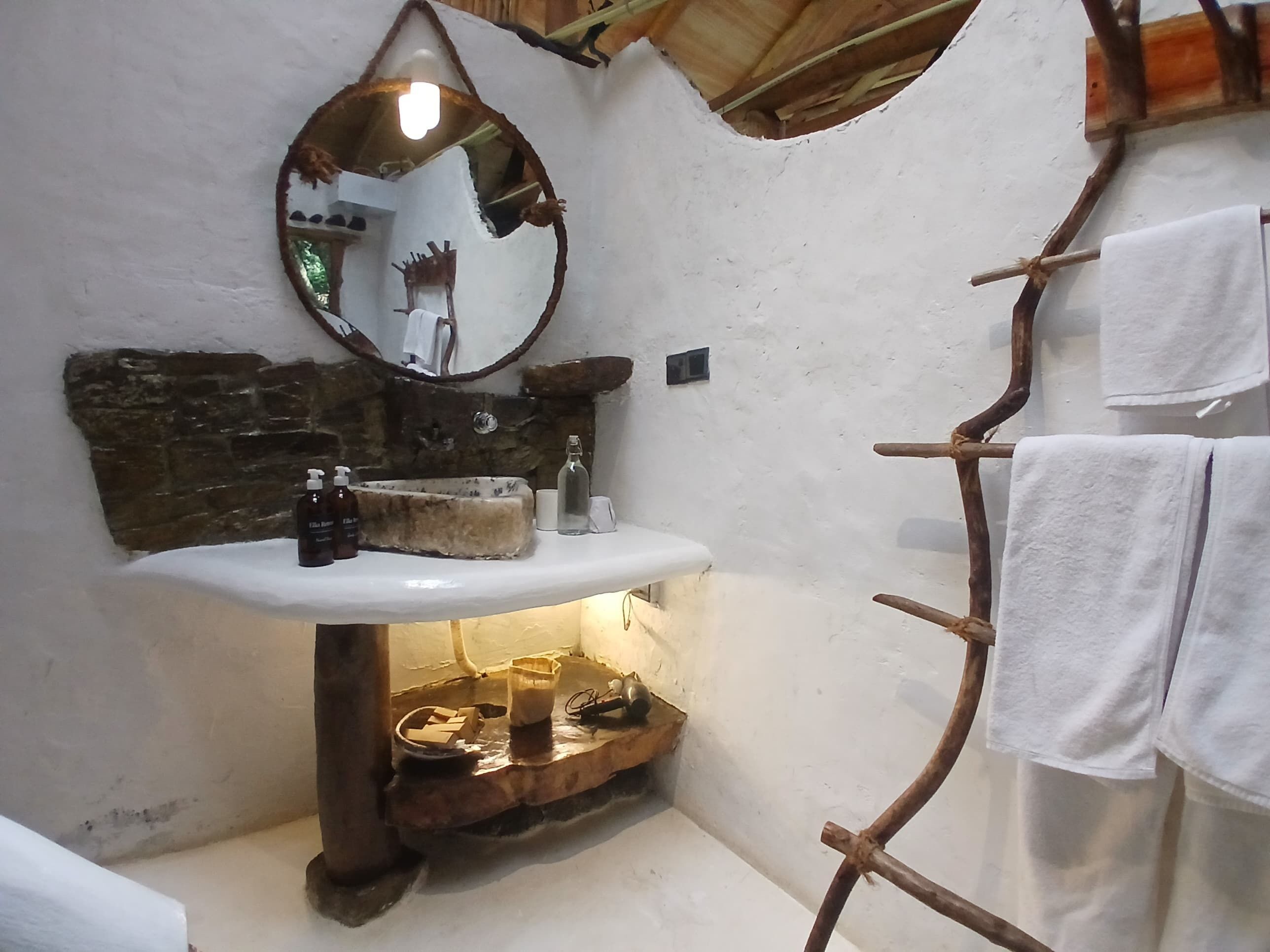 A rustic bathroom with a stone sink, a wooden shelf with toiletries, a mirror, and a towel rack.