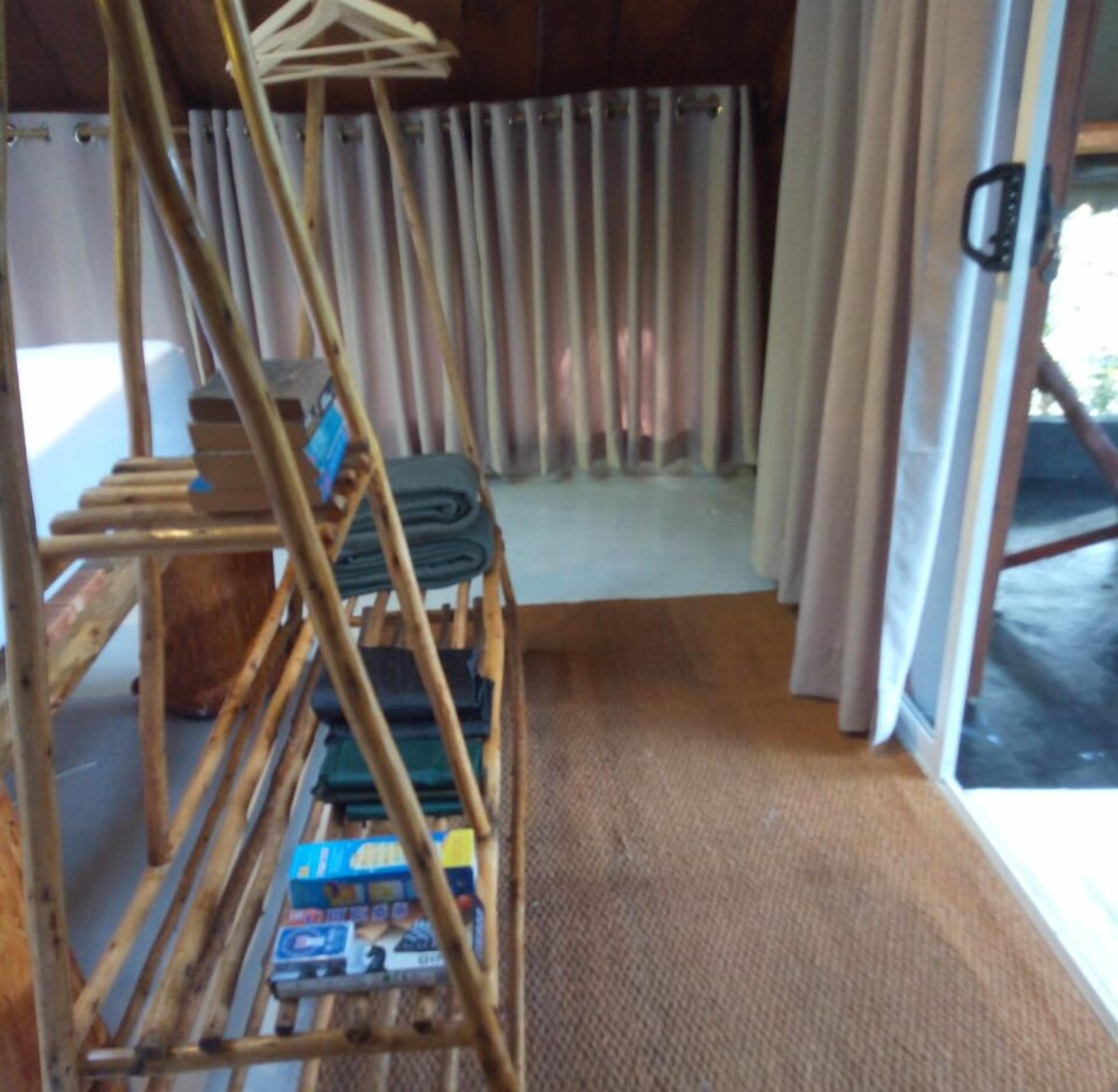 A room with a wooden rack holding folded clothes, a window with curtains, and a view of the outdoors.