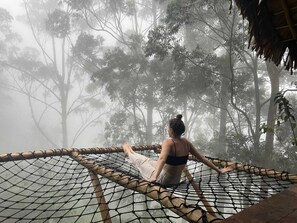 A person sitting on a hammock in a forested area with a thatched roof structure nearby. - Ella Retreat Hotel (Ella)