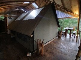 Una estructura rústica tipo tienda con techo inclinado, suelo de madera y una pequeña mesa con sillas en el exterior.