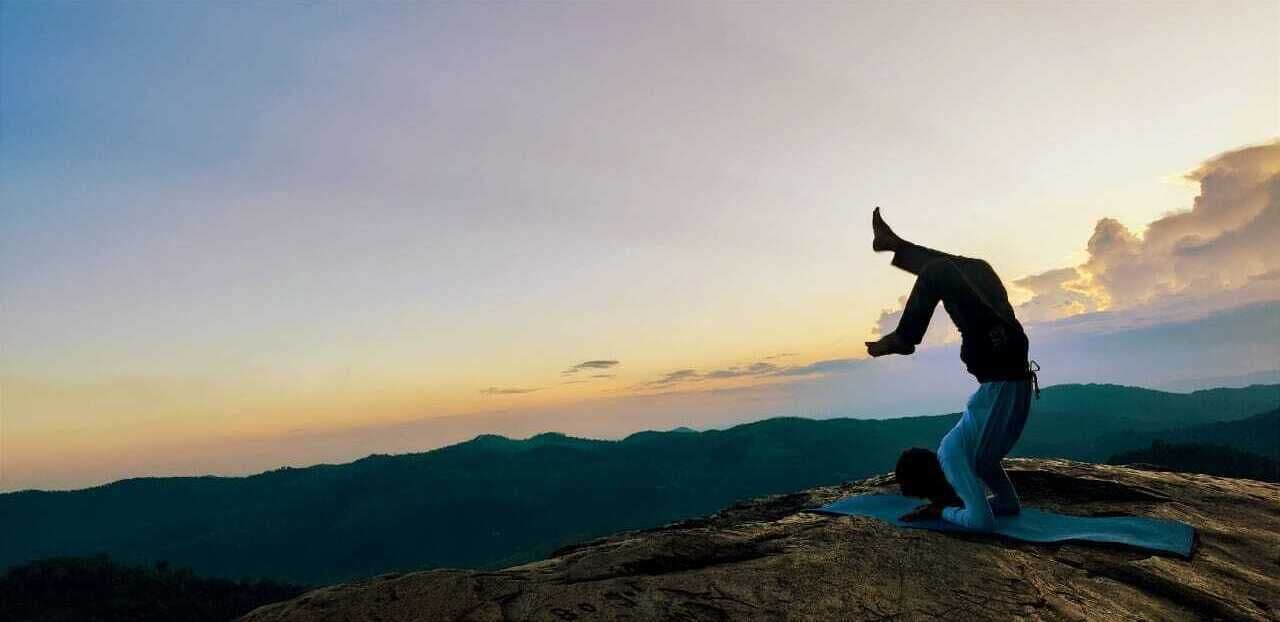 A person performing a yoga pose on a mat in a mountainous landscape.