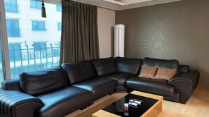 A modern living room with a sectional sofa, a glass coffee table, and a view of a building through large windows. - Home sweet home!!!!! (Pyeongtaek-si)