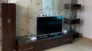 A modern living room with a marble wall, a flat-screen TV on a glass-top entertainment center, and a wooden cabinet. - Home sweet home!!!!! (Pyeongtaek-si)