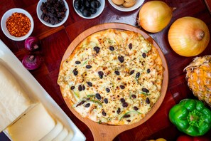 A pizza on a wooden board with various ingredients around it.