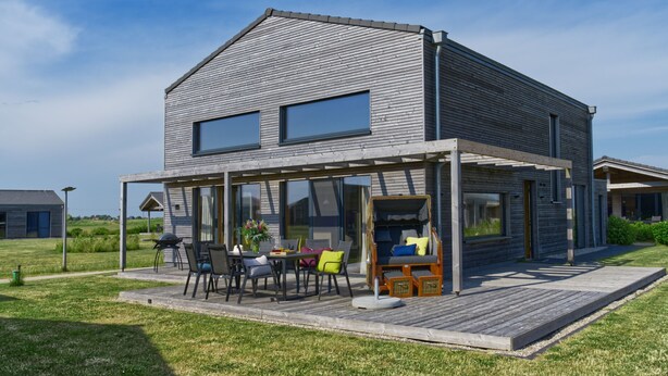 A modern house with a covered patio, large windows, and a well-maintained lawn. - (11) Gud Jard Chalet Großer Bär, Cat. FamilienZeit - Design holiday home Großer Bär (Pellworm)
