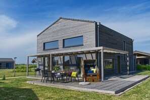 Ein modernes Haus mit überdachter Terrasse, großen Fenstern und einem gepflegten Rasen.