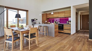 A modern kitchen with wooden cabinets, a central island, bar stools, and a dining area with a table and chairs. - (11) Gud Jard Chalet Großer Bär, Cat. FamilienZeit - Design holiday home Großer Bär (Pellworm)
