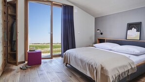 A bedroom with a bed, a wooden wardrobe, a purple ottoman, and a view of the outdoors. - (11) Gud Jard Chalet Großer Bär, Cat. FamilienZeit - Design holiday home Großer Bär (Pellworm)