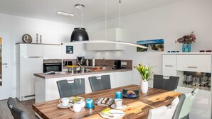 Una cocina moderna con armarios blancos, una mesa de comedor de madera y una lámpara colgante.