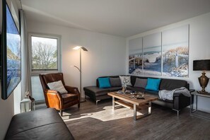 Un salon moderne avec un fauteuil en cuir, un canapé, une table basse et une grande fenêtre.