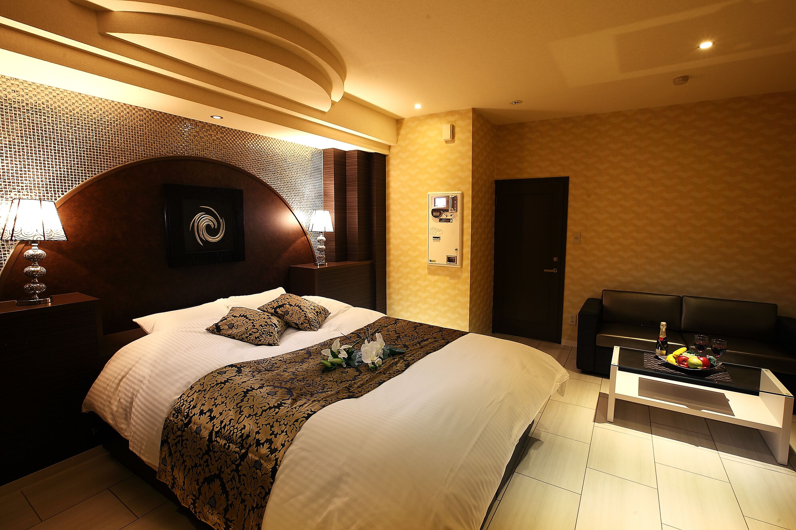 Une chambre d’hôtel avec un grand lit, un canapé, une table basse avec des fruits et un climatiseur fixé au mur.