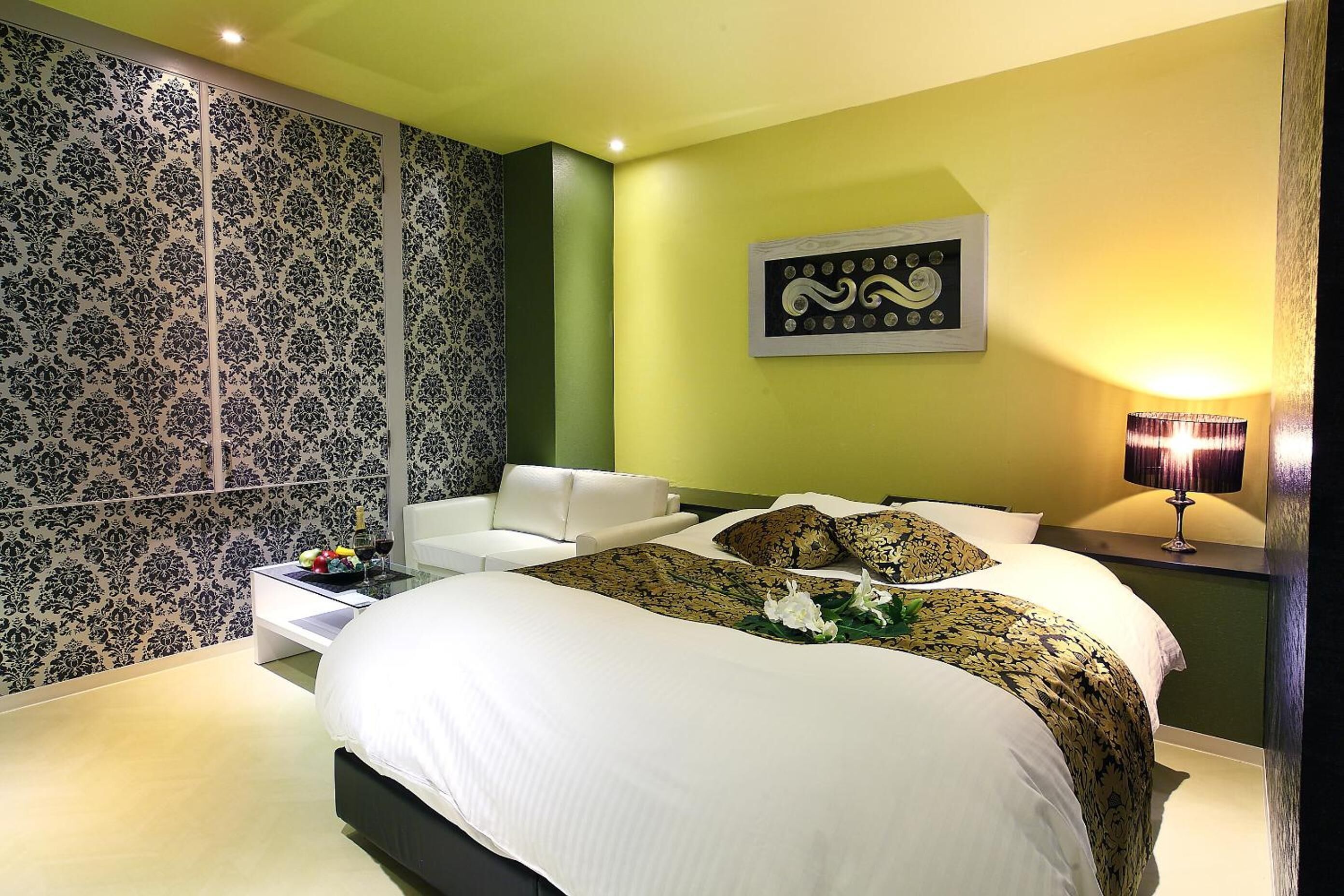A modern bedroom with a large bed, a nightstand with a lamp, and a decorative wall panel.