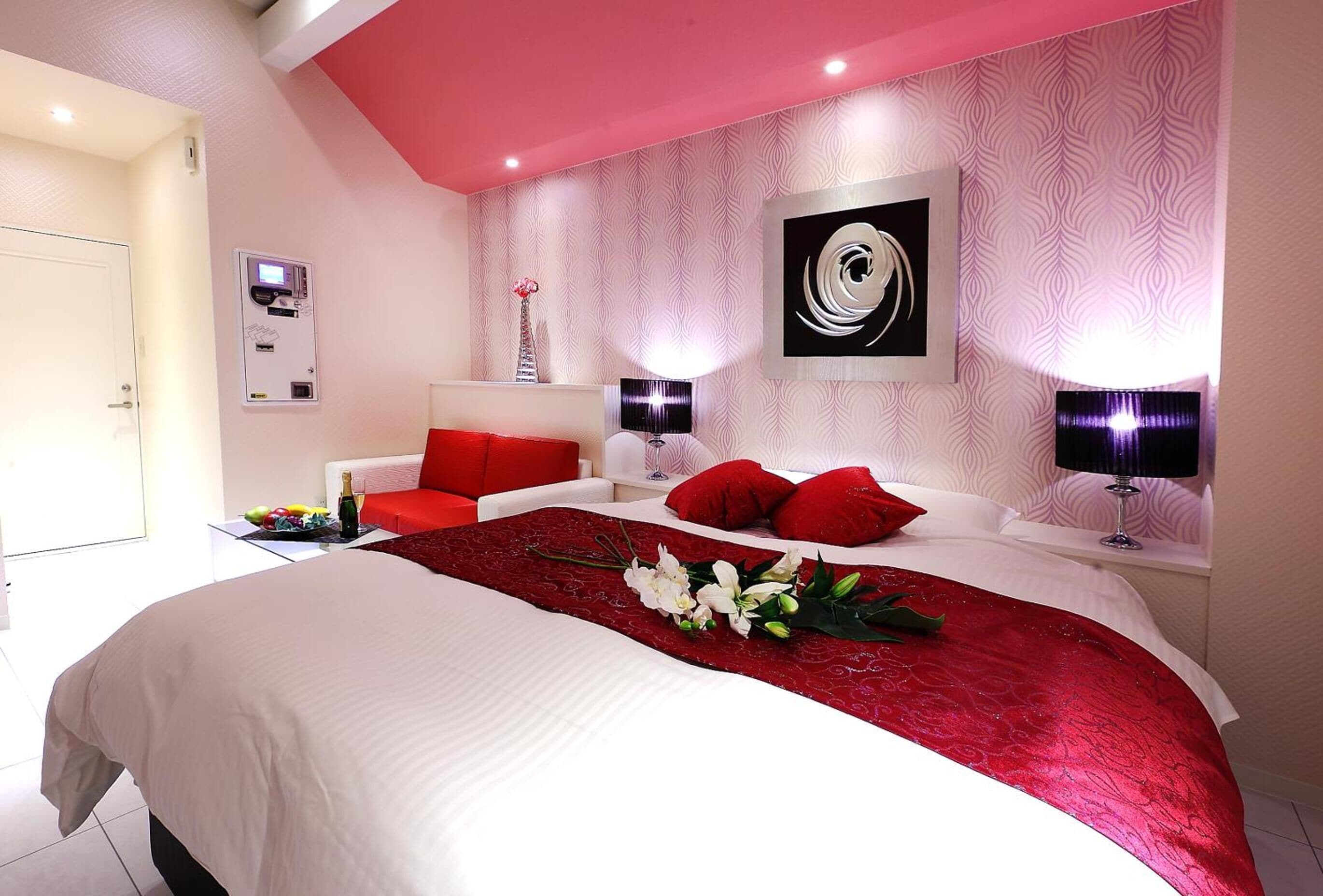 A modern hotel room with a large bed, red and white bedding, a red throw, and a bouquet of flowers.
