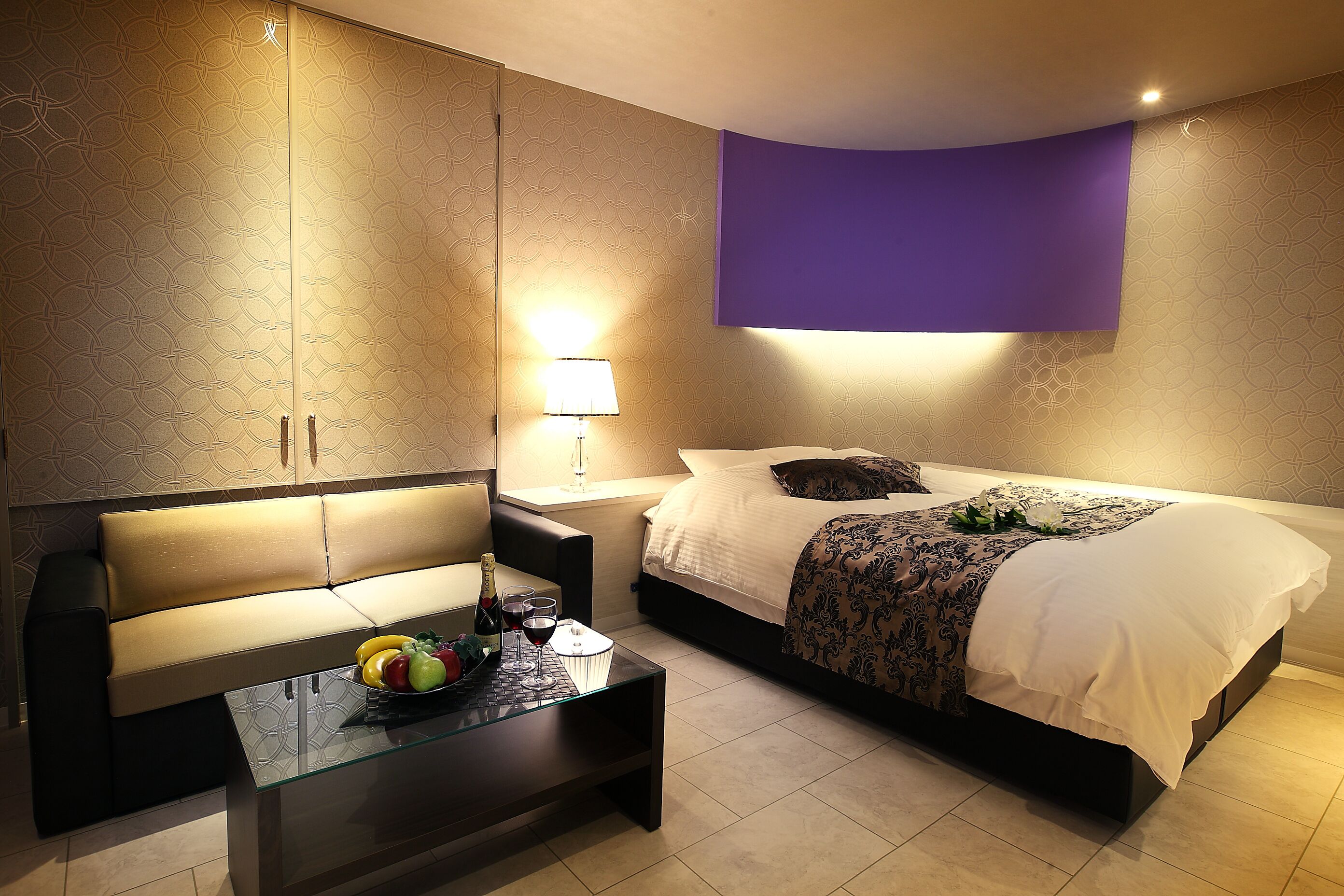 A modern bedroom with a bed, a sofa, a glass coffee table, and a nightstand with a lamp.