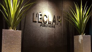 A reception area with a dark wall and the name 'L'ECOLE' prominently displayed. There are two potted plants on either side of the entrance. - Hotel L’eclair - Adults Only (Fukuyama)