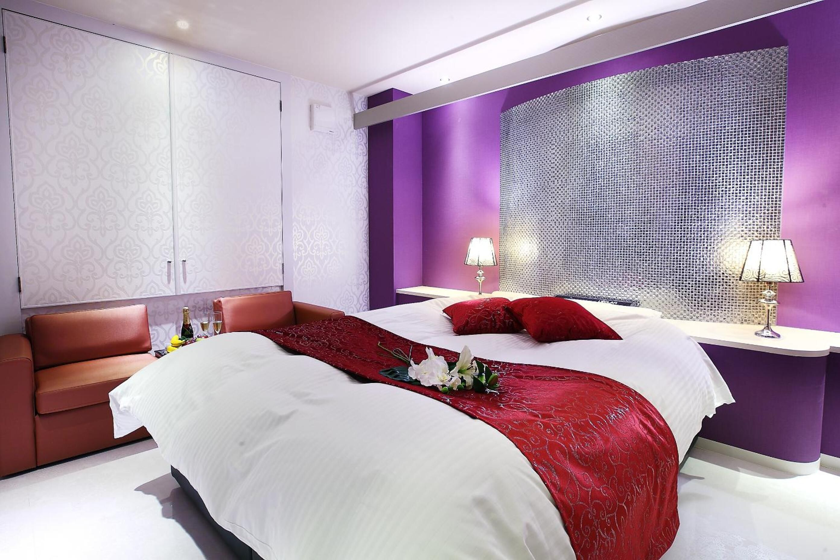 A modern hotel room with a large bed, a red throw blanket, and a decorative wall panel.