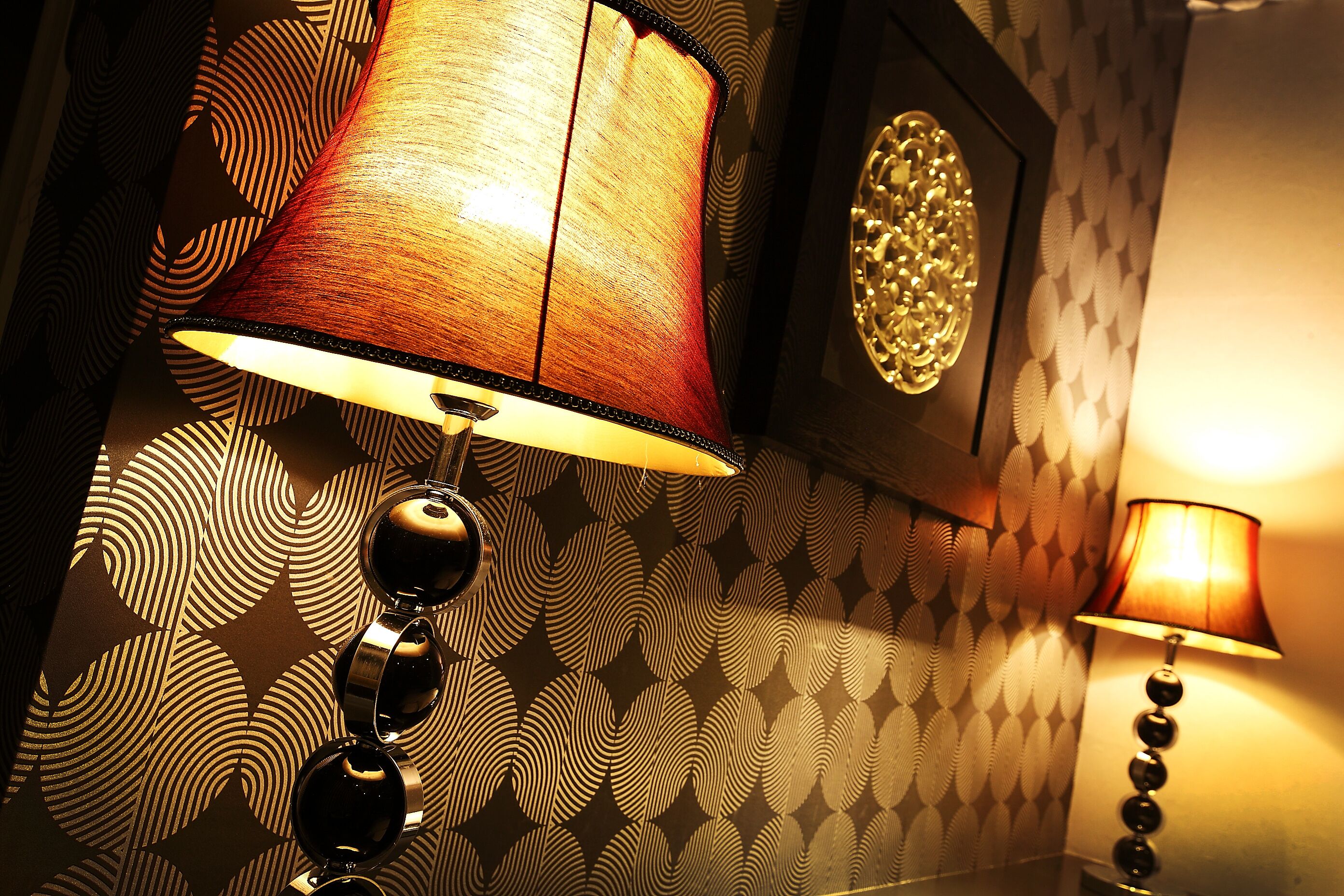 A wall with patterned wallpaper and two wall-mounted lamps.