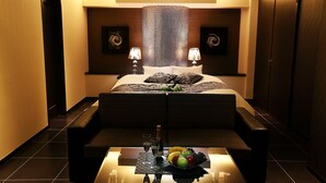 A modern hotel room with a large bed, two bedside lamps, a small table with a fruit bowl, and a bottle of champagne. - Hotel L’eclair - Adults Only (Fukuyama)