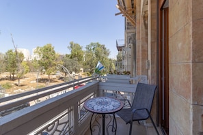 A balcony with a tiled table and chairs, overlooking a courtyard with trees and buildings. - Art apartment in Mamila (Jerusalem)