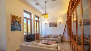 A spacious living room with a large window, a chandelier, and two sofas. - Art apartment in Mamila (Jerusalem)