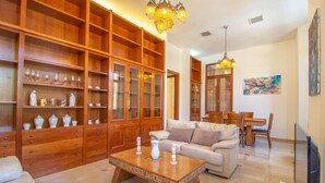 A spacious living room with a wooden cabinet, a beige sofa, a coffee table, and a dining area with a wooden table and chairs. - Art apartment in Mamila (Jerusalem)