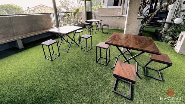 An outdoor seating area with tables and chairs, surrounded by greenery and concrete structures. - Haggai - Tourist Bangalow (Colombo)