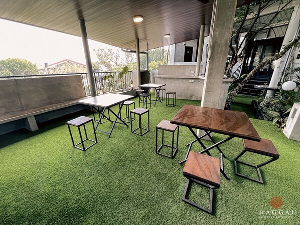An outdoor seating area with tables and chairs, surrounded by greenery and concrete structures. - Haggai - Tourist Bangalow (Colombo)