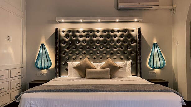 A modern bedroom with a tufted headboard, a large bed with multiple pillows, bedside lamps, and a built-in air conditioning unit. - Haggai - Tourist Bangalow (Colombo)