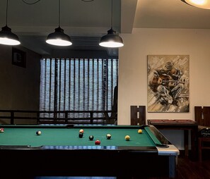 A pool table with balls, overhead lighting, a window with blinds, and a painting on the wall. - Haggai - Tourist Bangalow (Colombo)