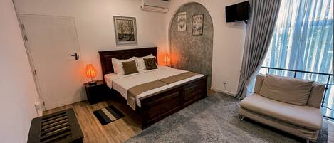 A bedroom with a bed, bedside lamps, a sofa, a TV, and a window with curtains.