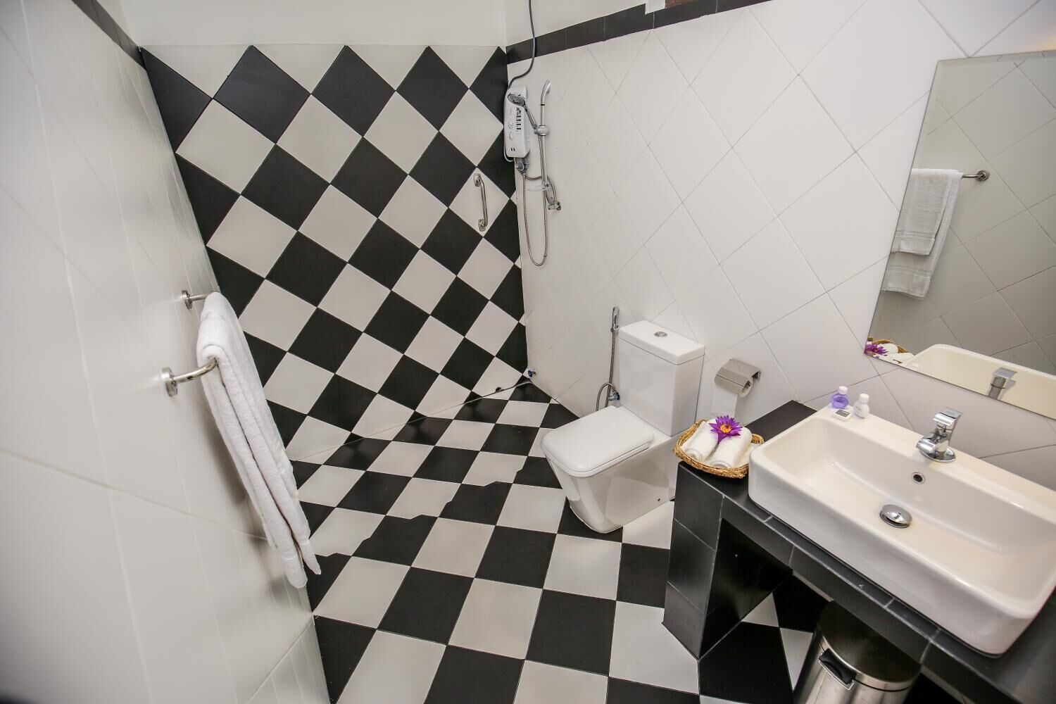 Un baño con piso a cuadros, inodoro, ducha, lavamanos y espejo.