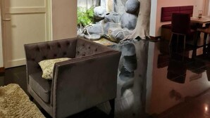 A living room with a grey sofa, a red chair, a decorative rock wall, and a dining area with a red sofa and table. - Haggai - Tourist Bangalow (Colombo)