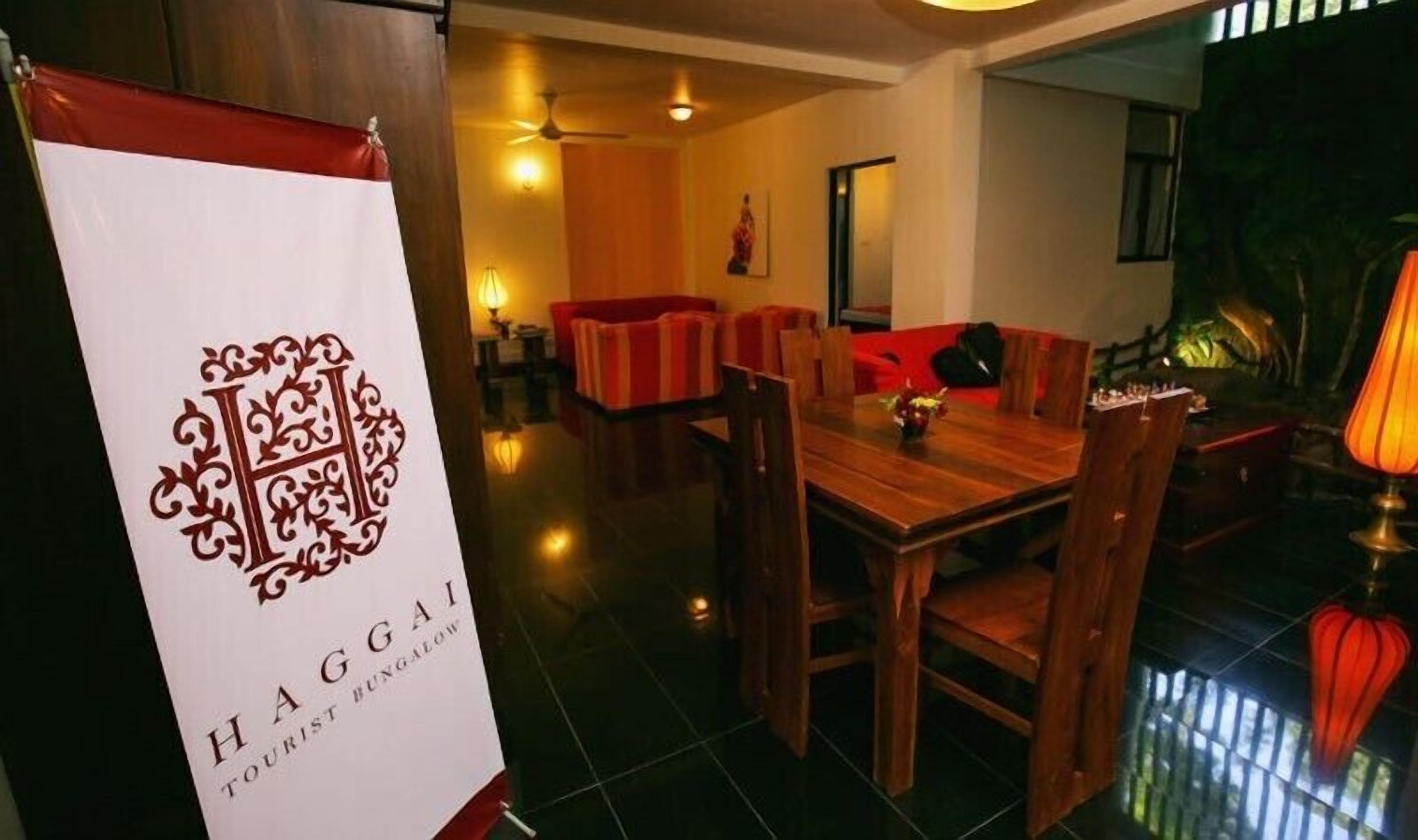 A dining area with a wooden table and chairs, a red-striped sofa, and a banner with a logo and text.