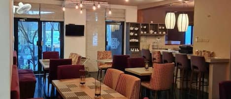 A restaurant with multiple dining tables and chairs, a bar area, and pendant lighting.