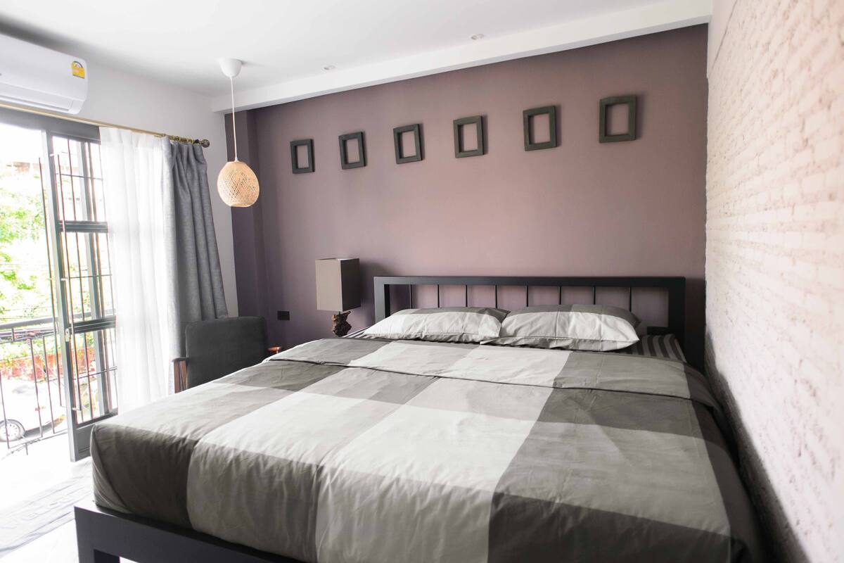 Un dormitorio con cama, una silla, una lámpara y una ventana con cortinas.