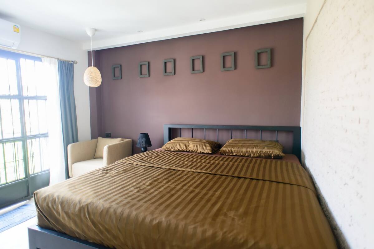 Un dormitorio con una cama grande, una silla, un escritorio y un ventanal con cortinas.