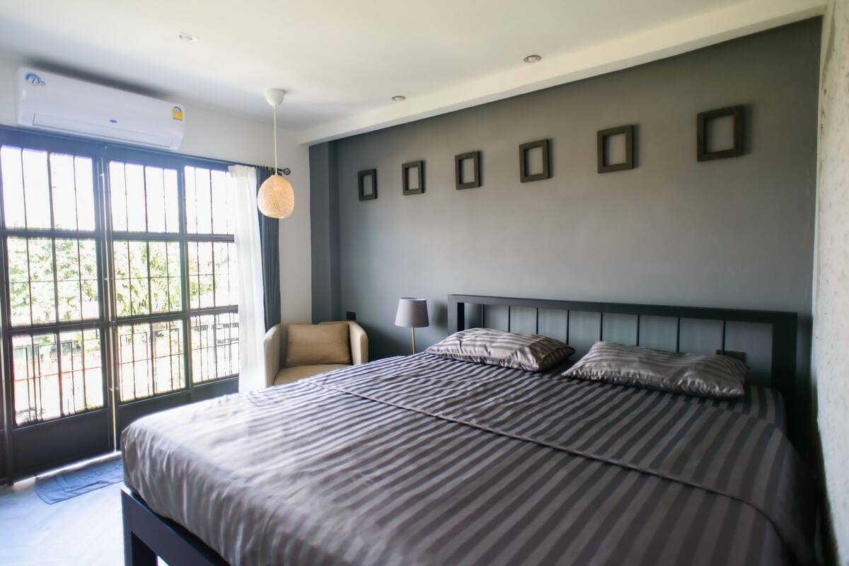 Un dormitorio moderno con una cama grande, una silla y una ventana con vistas a árboles.